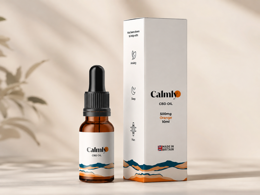 A bottle of Calmio CBD Oil next to its white packaging box, featuring a minimalist orange and blue mountain design on a warm beige background with soft leaf shadows.